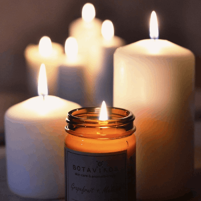 6 pillar candles with flames burning and a jarred candle at the front